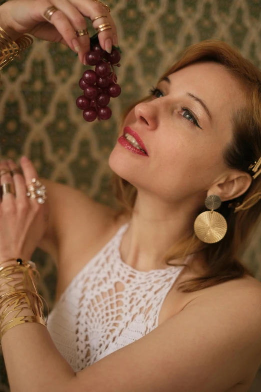 a woman in a white dress holding a bunch of grapes, inspired by Leila Faithfull, bone jewellery, gold earring, maria panfilova, gold and red