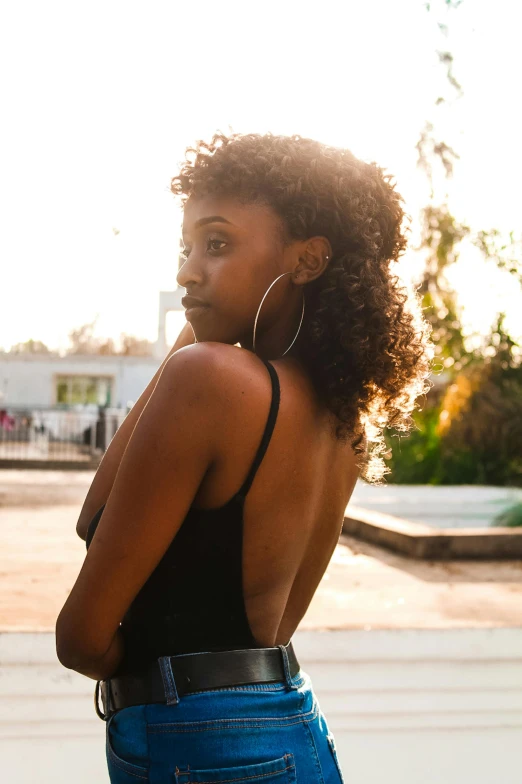 a woman in a black top and blue jeans, by Niko Henrichon, trending on pexels, renaissance, ebony skin, looking off into the sunset, arched back, poolside