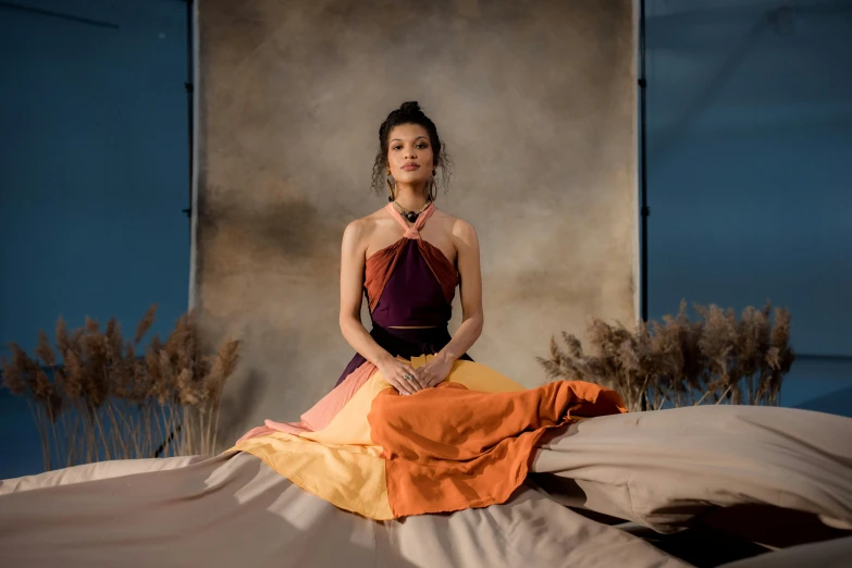 a woman in a dress sitting on a bed, inspired by Tang Di, trending on pexels, conceptual art, festival of rich colors, skies behind, asian woman, colour blocking