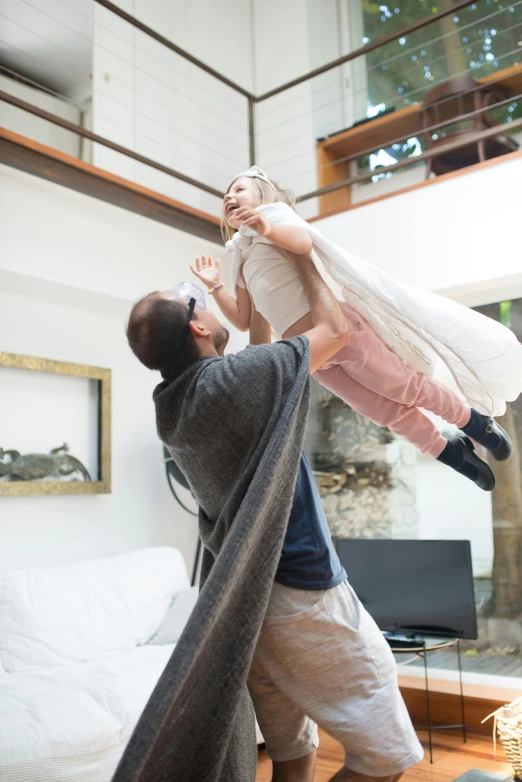 a man holding a child up in the air, with cape, at home, grey, full body hero