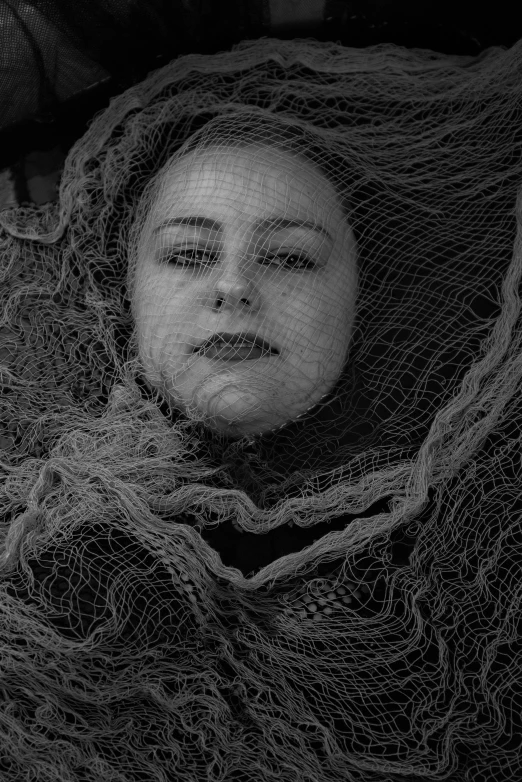 a black and white photo of a woman wrapped in a net, inspired by Kati Horna, tired haunted expression, max dennison, show, judy boyle intricate