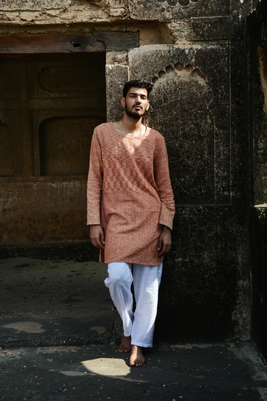 a man standing in front of a stone building, inspired by Sunil Das, renaissance, wearing a kurta, terracotta, streetwear, brown