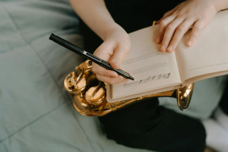 a person holding a pen and writing on a book, an album cover, by Julia Pishtar, trending on pexels, brass instruments, 15081959 21121991 01012000 4k, schools, quiet beauty