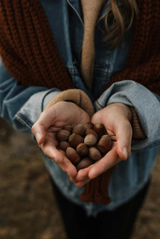 a woman holding a handful of nuts in her hands, by Jesper Knudsen, pexels contest winner, hearts, puffballs, sydney hanson, brown clothes