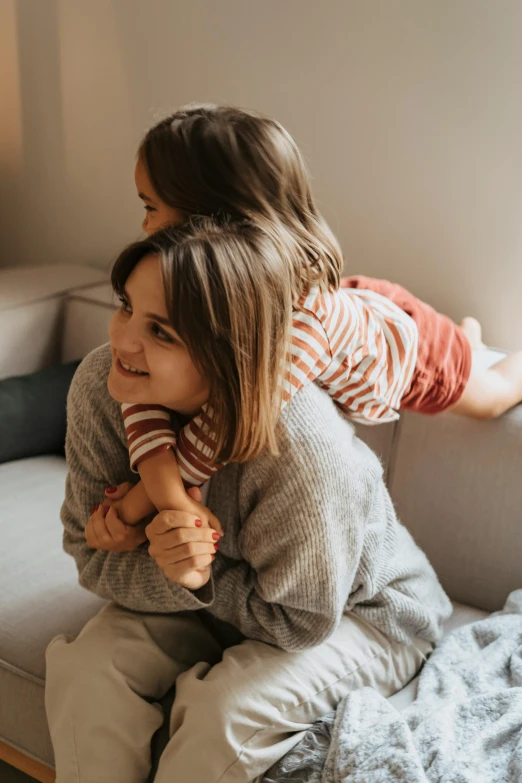 a woman sitting on top of a couch next to a little girl, pexels contest winner, incoherents, holding each other, kids playing, profile image, laying on her back