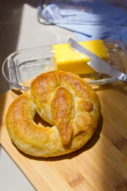 a couple of pretzels sitting on top of a wooden cutting board, butter, rondel, bruce kaiser, (cheese)