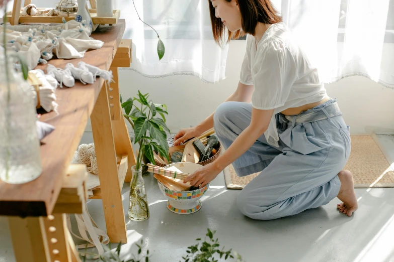 a woman sitting on the floor next to a potted plant, by Julia Pishtar, pexels contest winner, cutting a salad, japanese collection product, painted overalls, clean and organized