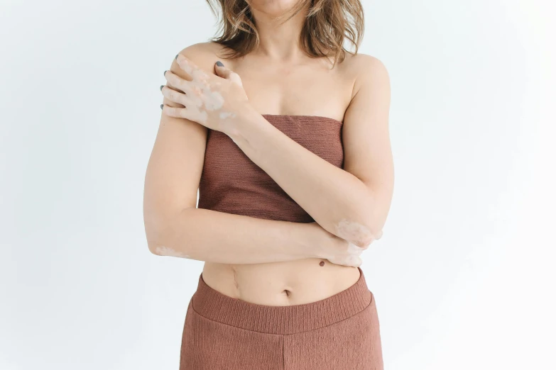 a woman standing with her arms folded over her chest, trending on pexels, rotting clay skin, manuka, wearing a cropped top, synthetic skin