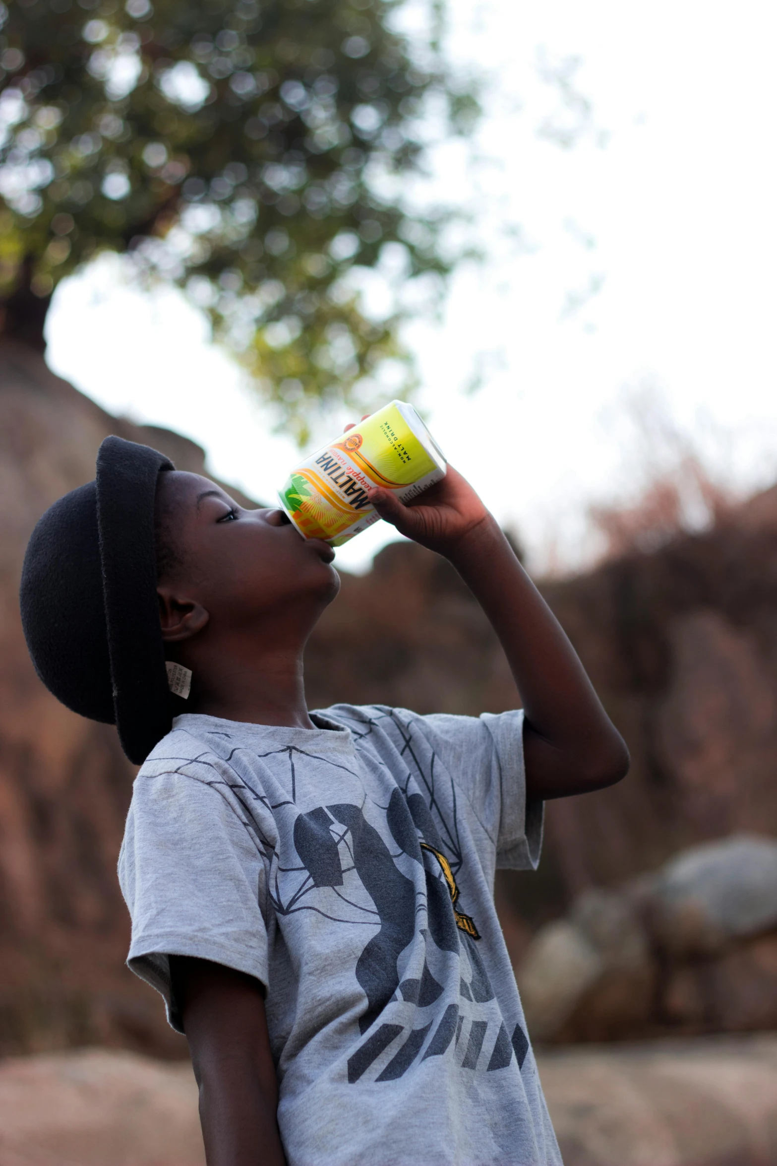 a young boy drinking from a plastic bottle, by Adam Manyoki, energy drink, baobab tree, mustard, cans