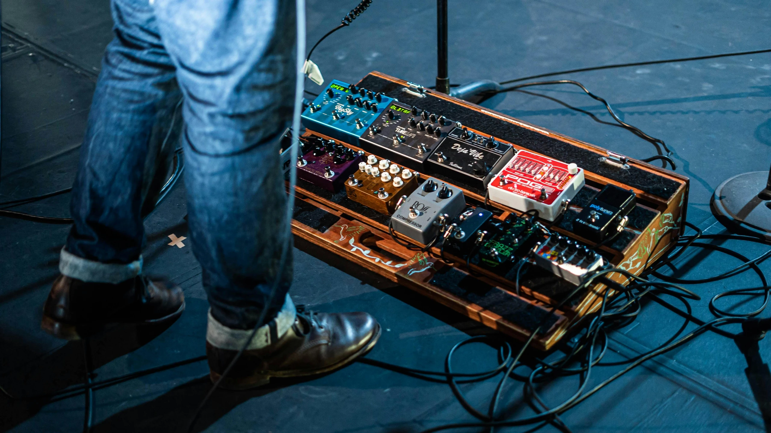 a person standing next to a guitar on a stage, by Joe Bowler, unsplash, modular synth, detailed foot shot, on a wooden tray, lachlan bailey