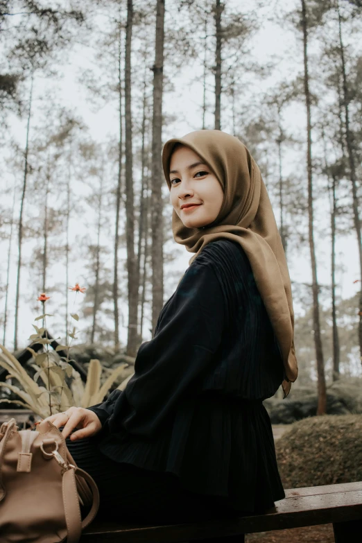 a woman sitting on top of a wooden bench, inspired by Nazmi Ziya Güran, pexels contest winner, sumatraism, wrapped in a black scarf, in front of a forest background, portrait of a cute woman, desaturated