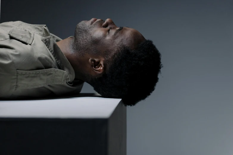 a man laying on top of a white box, by Clifford Ross, pexels contest winner, hyperrealism, dark skinned, looking off to the side, halo above head, ignant
