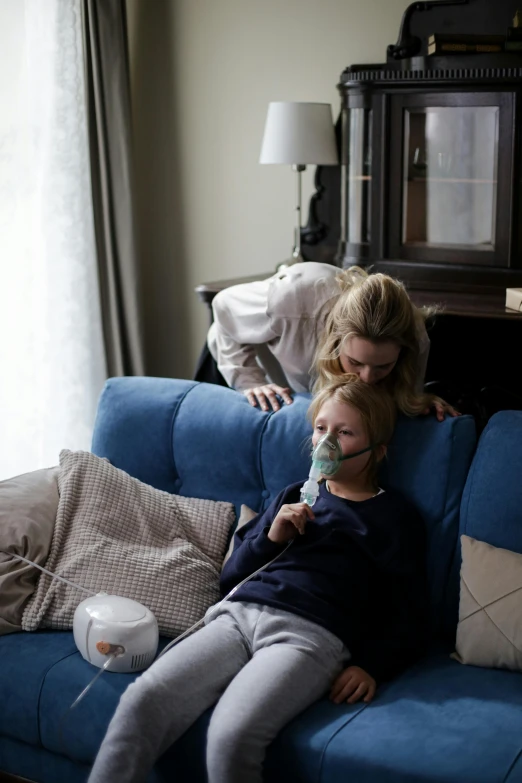 a woman sitting on top of a blue couch next to a little girl, oxygen mask, cosy atmoshpere, facemask, grey