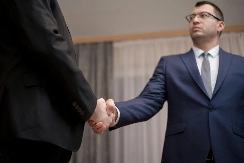 two men in suits shaking hands in front of a curtain, pexels contest winner, looking threatening, people at work, фото девушка курит, wearing a suit and glasses