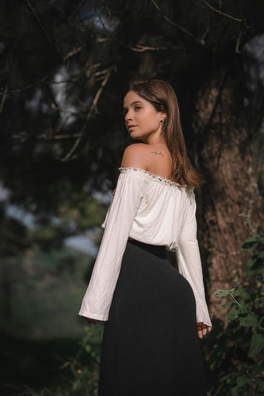 a woman standing in front of a tree, by Alejandro Obregón, pexels contest winner, renaissance, off the shoulder shirt, at a fashion shoot, bells, back