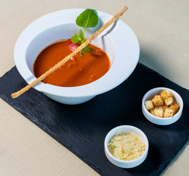 a bowl of soup sitting on top of a black tray, inspired by Antonio Rotta, venetian red, restaurant, high quality product image”