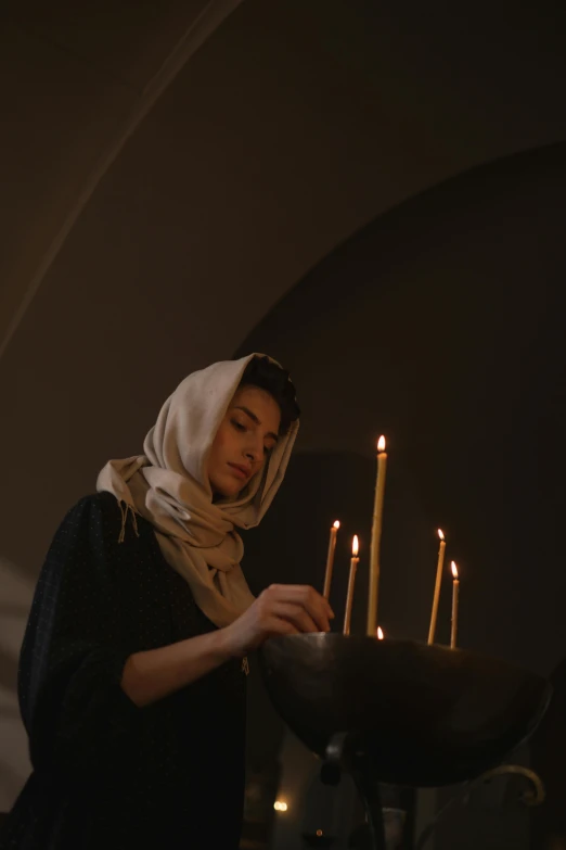 a woman lighting candles in a dark room, trending on unsplash, renaissance, wearing a head scarf, in a church. medium shot, minimalist, movie still