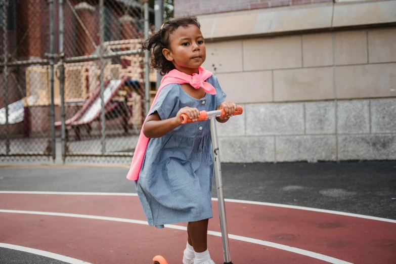 a little girl riding a scooter on a playground, by Lily Delissa Joseph, holding a cane, denim, wearing a dress, humans of new york