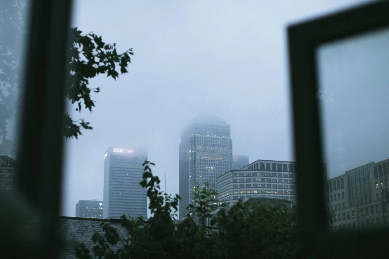 a view of a city through a window, inspired by Elsa Bleda, unsplash contest winner, realism, under a gray foggy sky, canary wharf, city buildings on top of trees, humid evening