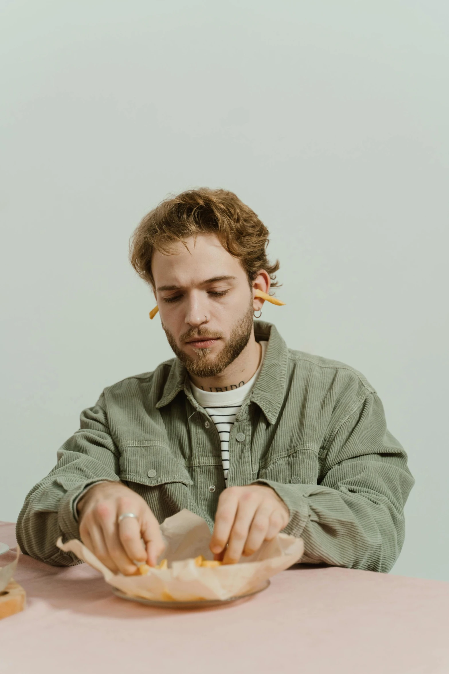 a man sitting at a table with a plate of food, a colorized photo, by artist, trending on pexels, hyperrealism, orange metal ears, post malone, on a gray background, in an action pose