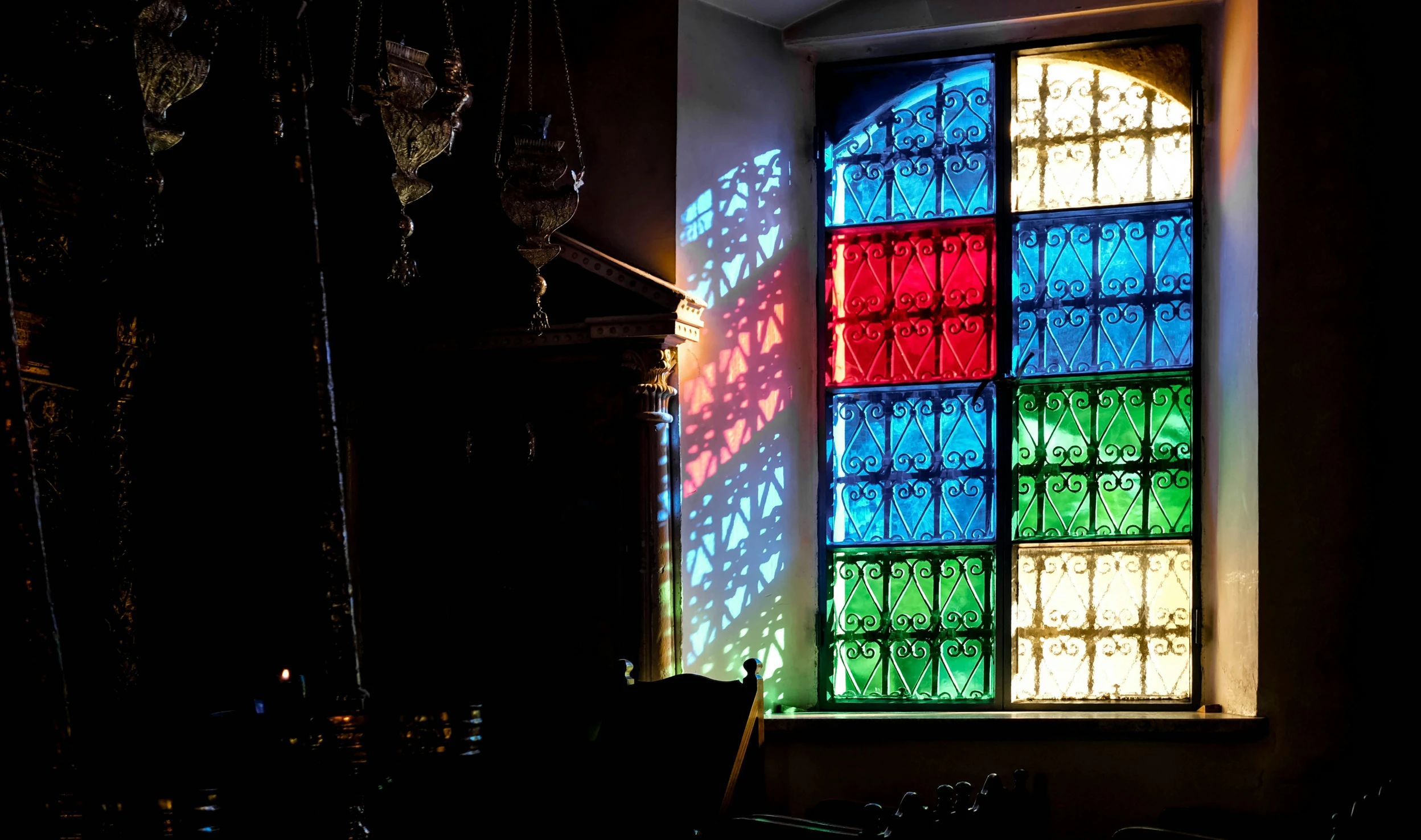 a stained glass window in a dark room, a photo, by Julia Pishtar, multicoloured, afternoon sunlight, mosque synagogue interior, cast shadows