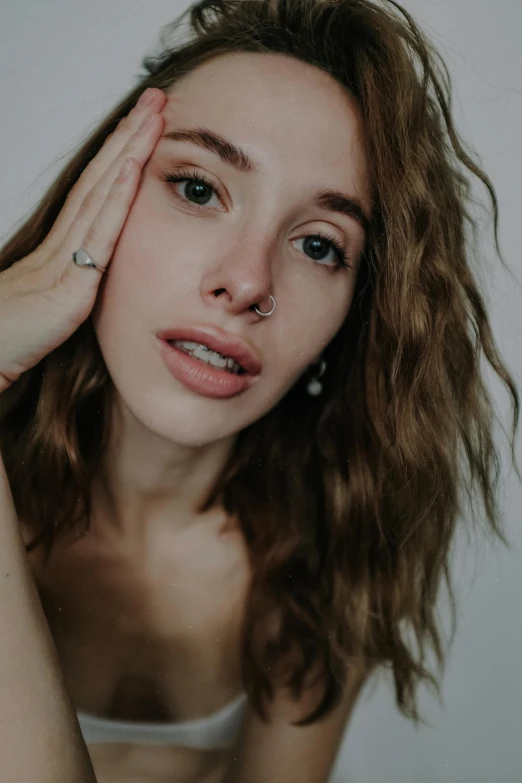 a beautiful young woman posing for a picture, inspired by Elsa Bleda, trending on pexels, photorealism, nose piercing, no makeup wavy hair, hand on cheek, pale thin lips