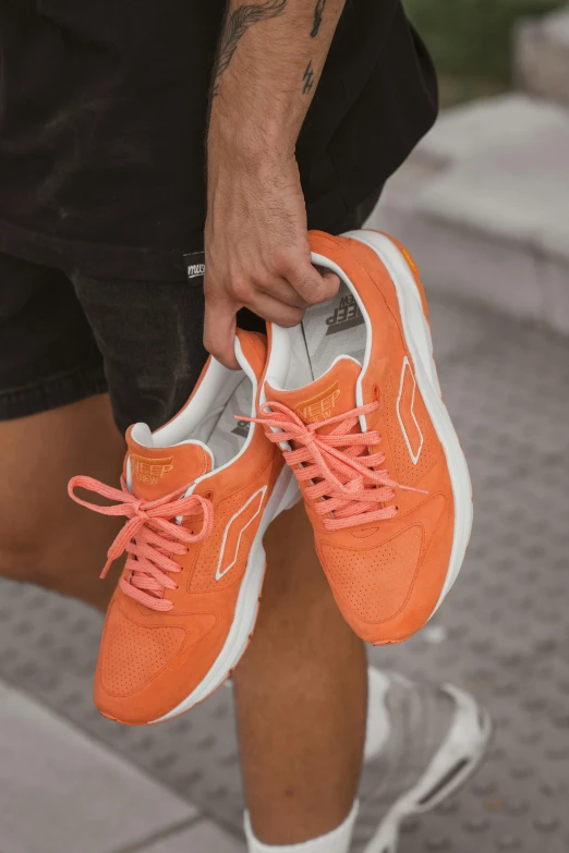 a man holding a pair of orange sneakers, lumi, less detailing, reefs, kangaroos