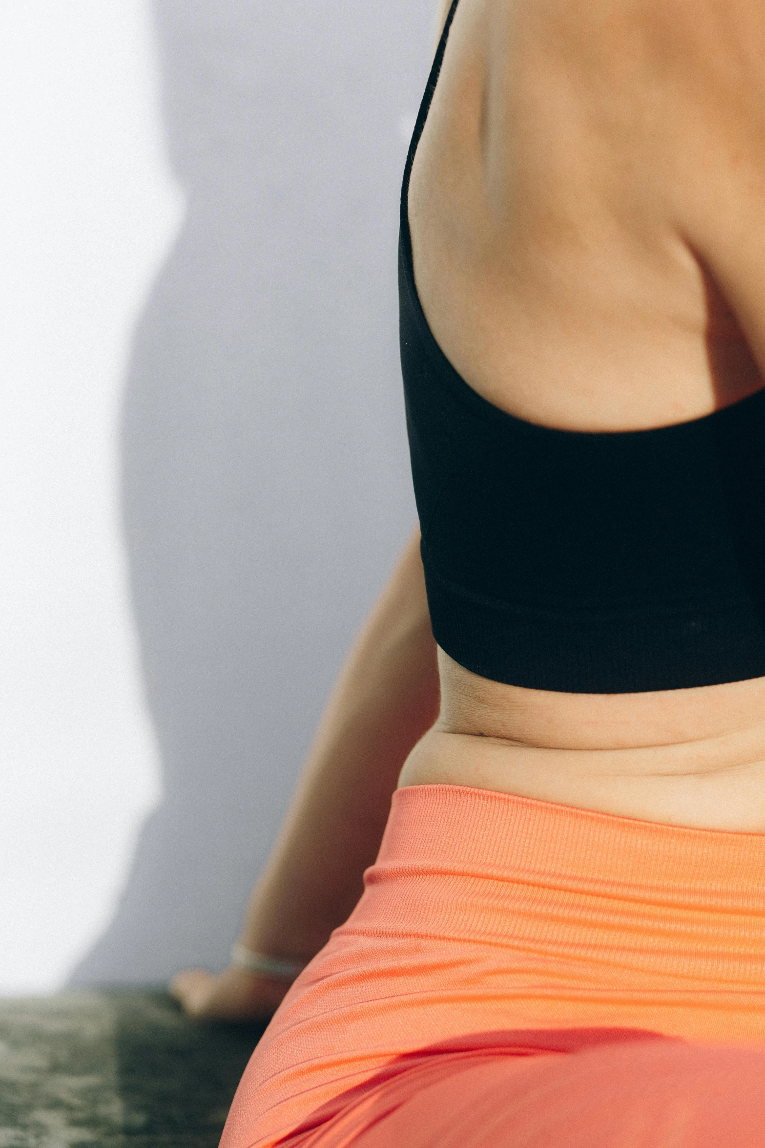 a woman in a black top and orange skirt, trending on pexels, detailed sports bra, facing away from camera, light on top, hyperedetailed photo