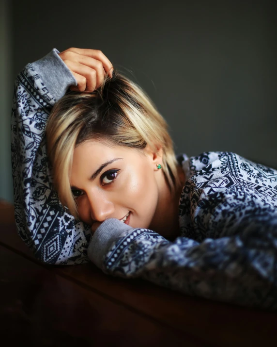 a woman laying on top of a wooden table, a colorized photo, trending on pexels, hurufiyya, wearing casual sweater, short platinum hair tomboy, portrait of ana de armas, jessica nigri