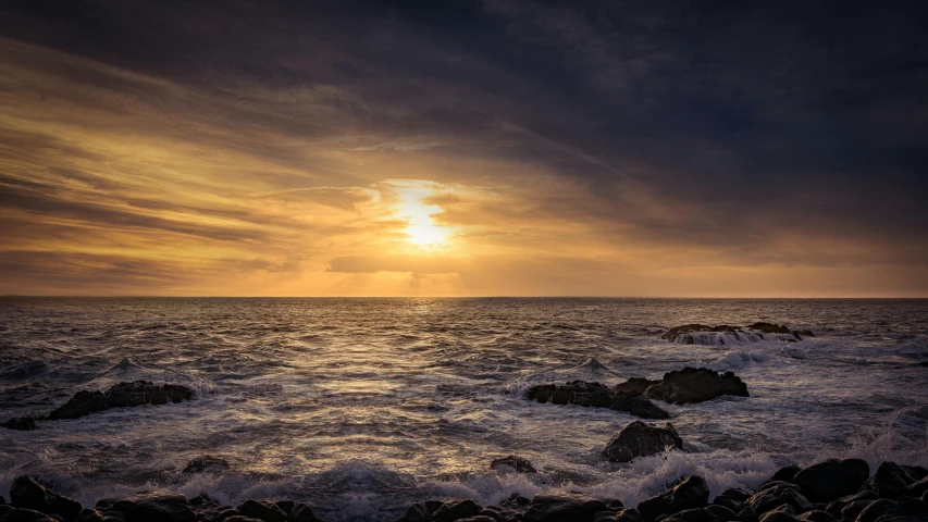 a sunset over the ocean with rocks in the foreground, pexels contest winner, maryport, rough seas, sunset panorama, grey