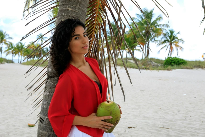 a woman standing next to a palm tree on a beach, an olive skinned, latina, coconuts, portrait image