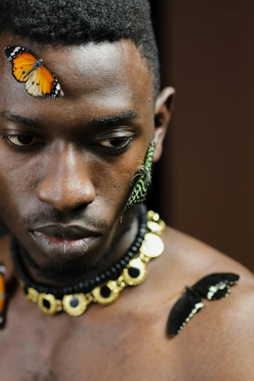 a man with a butterfly on his forehead, an album cover, trending on pexels, afrofuturism, snake human hybrid, adut akech, tribal jewelry, lgbtq