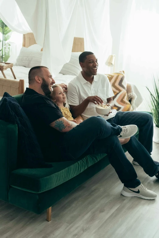 a group of people sitting on top of a green couch, watching tv, lgbtq, husband wife and son, rectangle