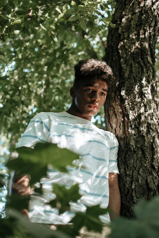 a young man standing next to a tree, by Andrew Stevovich, unsplash, visual art, black teenage boy, under the soft shadow of a tree, ((trees)), teddy fresh