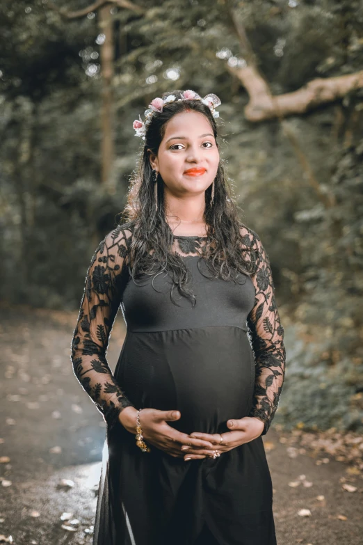 a pregnant woman in a black dress standing on a path in the woods, pexels contest winner, with kerala motifs, portrait image, promo image, maternal