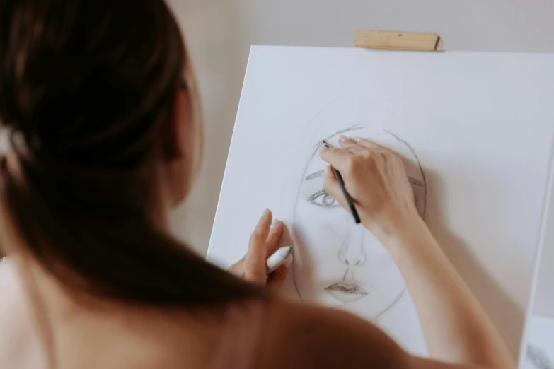 a woman is drawing a woman's face on a piece of paper, a drawing, by Emma Andijewska, trending on pexels, analytical art, painting a canvas, head and waist potrait, professional drawing, on canvas