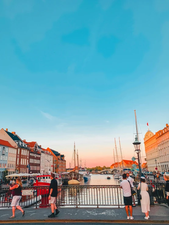 a group of people walking across a bridge next to a body of water, by Sebastian Spreng, pexels contest winner, brightly colored buildings, denmark, at the golden hour, slide show