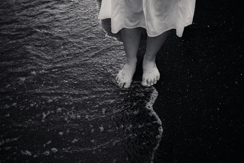 a black and white photo of a person standing in the water, by Lucia Peka, unsplash, renaissance, barefeet, black sand, 15081959 21121991 01012000 4k, wearing a dress made of water