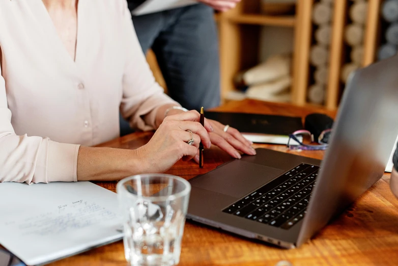 a woman sitting at a table using a laptop computer, by Carey Morris, trending on pexels, bottom angle, pen and paper, avatar image, brown