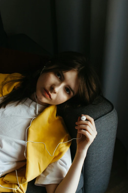 a woman laying on a couch with headphones on, inspired by Elsa Bleda, trending on pexels, realism, yellow robe, portrait of depressed teen, 🤤 girl portrait, elegant pose