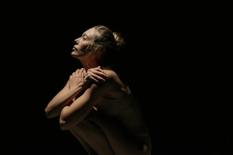 a nude woman standing in front of a black background, a portrait, unsplash, contemporary dance, hugging her knees, sunlit, sitting