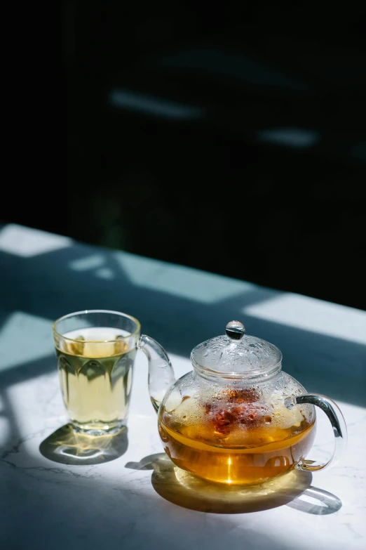 a cup of tea and a teapot on a table, unsplash, iced tea glass, slide show, sun dappled, half image