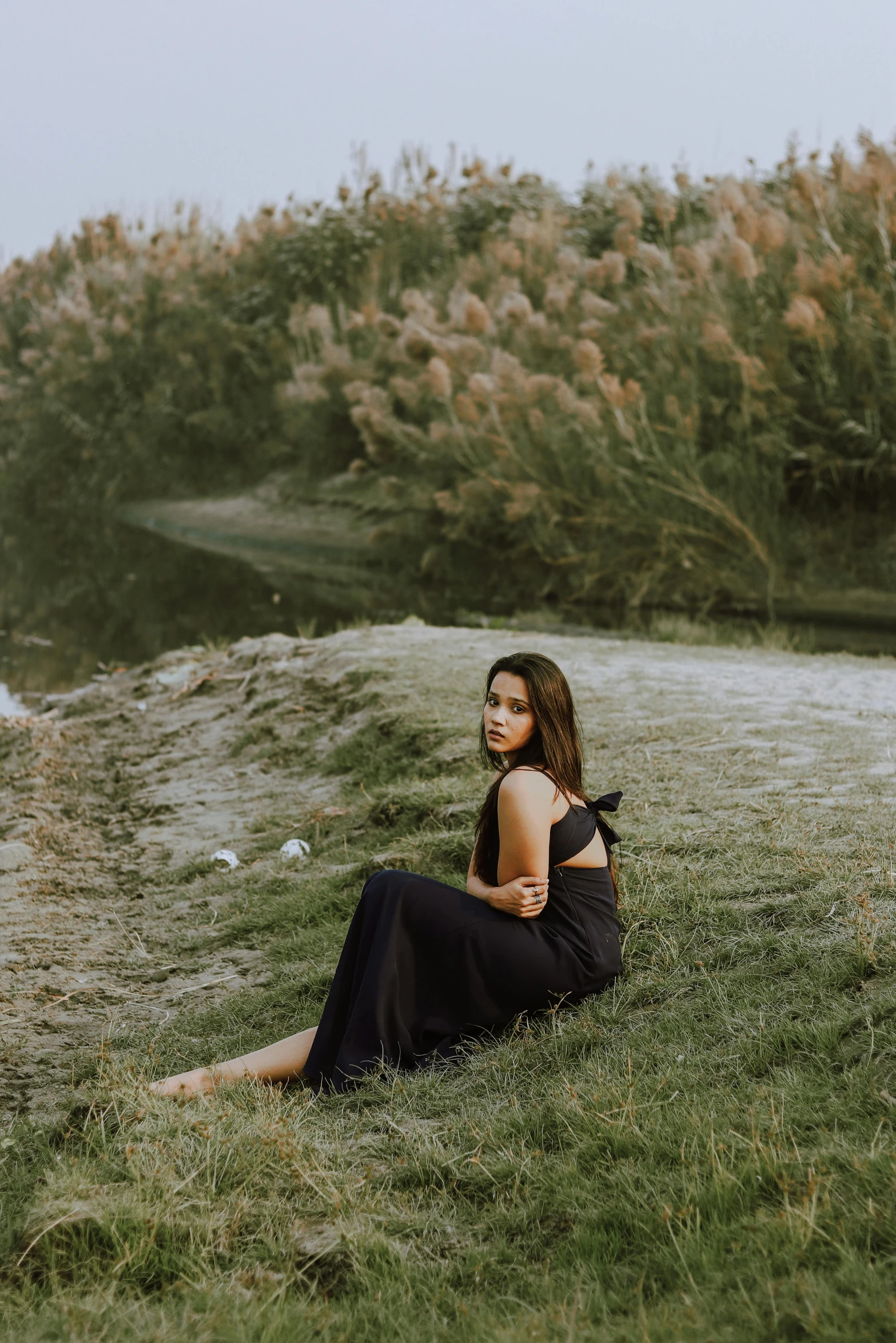 a woman in a black dress sitting next to a body of water, in the grass, indian girl with brown skin, profile image, 2019 trending photo