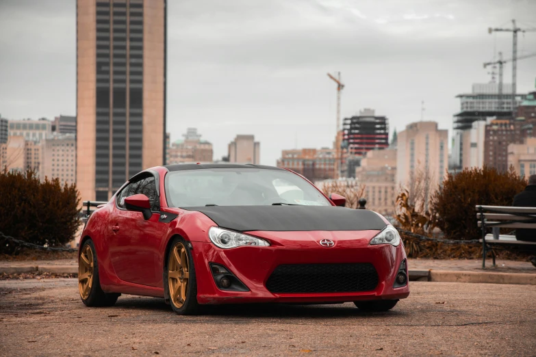 a red sports car parked in a parking lot, by Jason Felix, pexels contest winner, renaissance, red gold black, 2013 scion tc, with a city in the background, 2 5 6 x 2 5 6