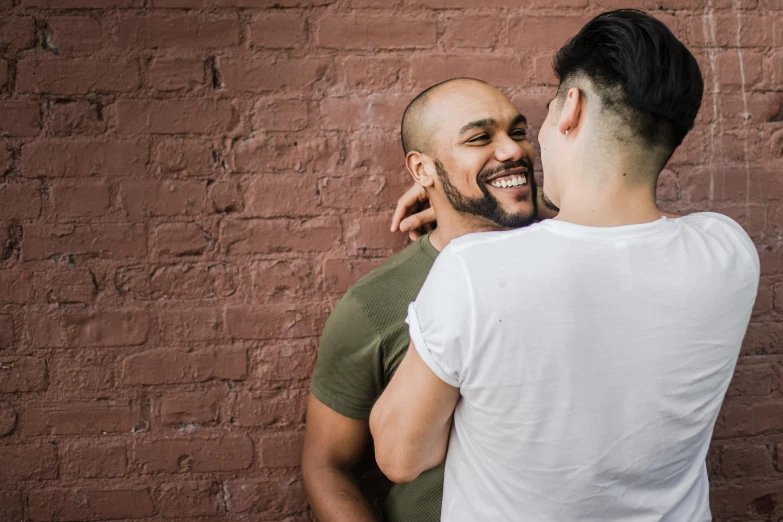 a man standing next to a woman in front of a brick wall, by Meredith Dillman, pexels contest winner, two men hugging, mix of ethnicities and genders, gay, background image