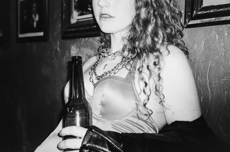 a black and white photo of a woman holding a beer, inspired by Nan Goldin, tumblr, renaissance, wearing chains, publicity cosplay, black leather bra, curly