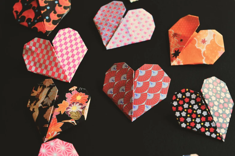 a bunch of origami paper hearts on a table, sōsaku hanga, pop motifs, warm coloured, with a black background, close ups