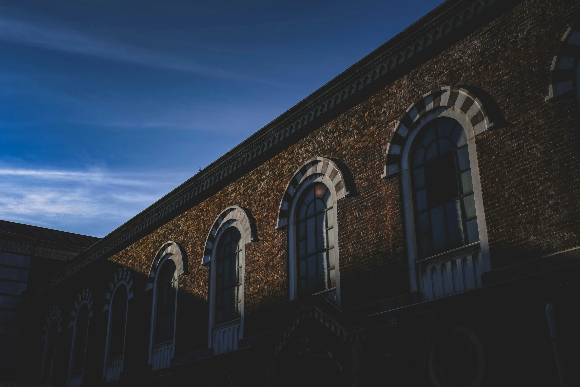 a tall brick building sitting under a blue sky, an album cover, unsplash contest winner, renaissance, dark moody backlighting, background image, khedival opera house, windows and walls :5