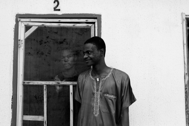 a black and white photo of a man standing in front of a door, by Kristian Zahrtmann, pexels contest winner, realism, wearing an african dress, prisoner, two people, smiling male