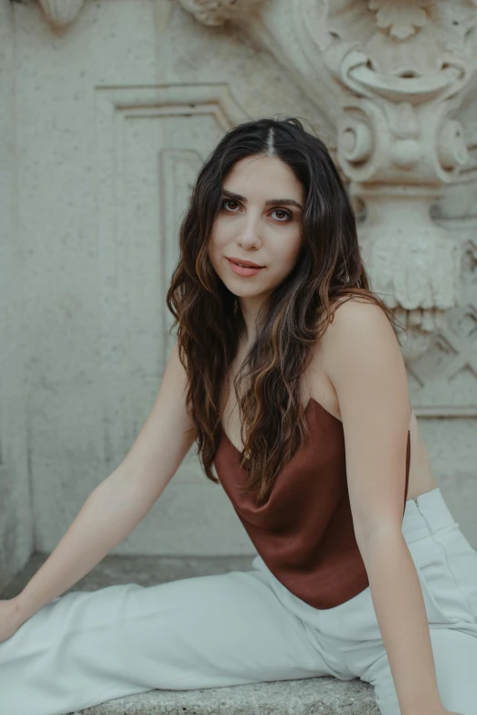 a woman sitting on the steps of a building, an album cover, inspired by Lucia Peka, trending on pexels, art nouveau, brown colored long hair, beautiful jewish woman, solid background, wearing a camisole